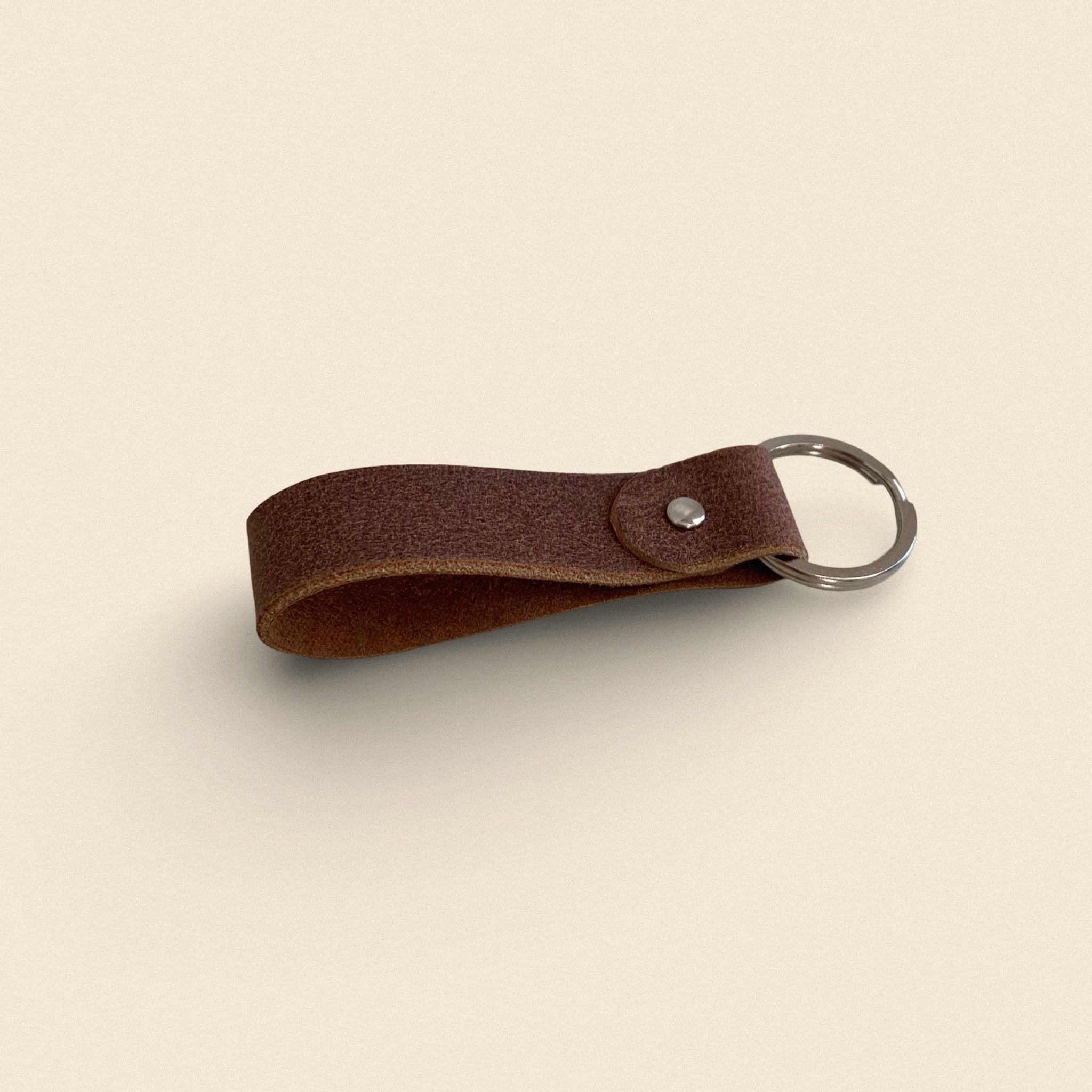 17. Dark brown handmade leather keychain by Yoru with metal ring on beige background