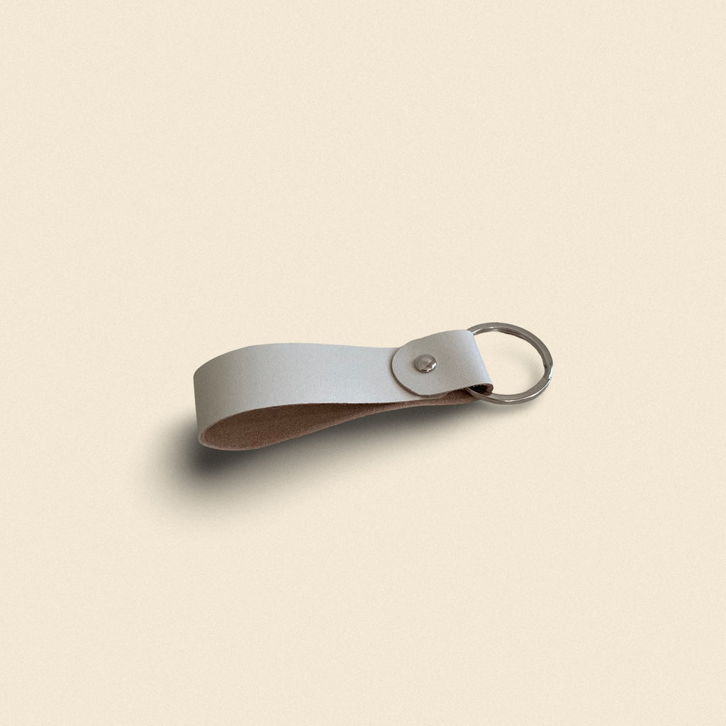 12. White handmade leather keychain by Yoru with metal ring on beige background