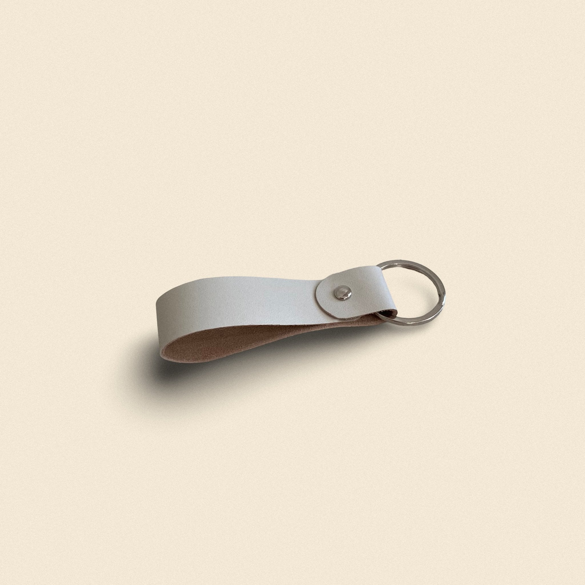 12. White handmade leather keychain by Yoru with metal ring on beige background
