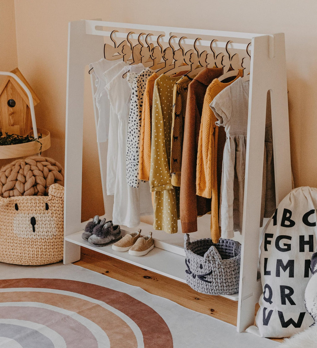 7. White toddler clothing rack with neutral-toned children's clothes in a cozy room setting