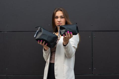 2. Woman displaying two Zelma Kraft black leather cosmetic bags, highlighting versatile sizes