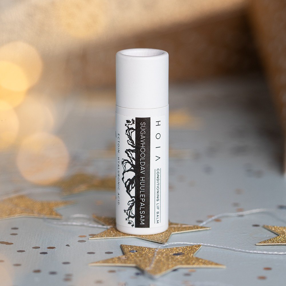 1. HOIA homespa Conditioning Lip Balm with Ectoin in white tube on festive background with gold stars, featuring black tree design and text highlighting ectoin and hyaluronic acid ingredients.
