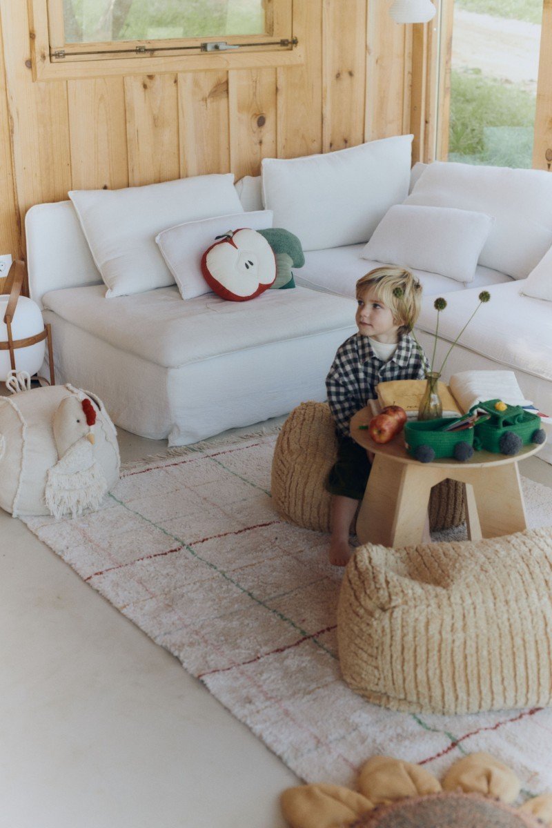 1. Child sitting on natural multicolor striped rug in cozy living room with white sofa and wooden table