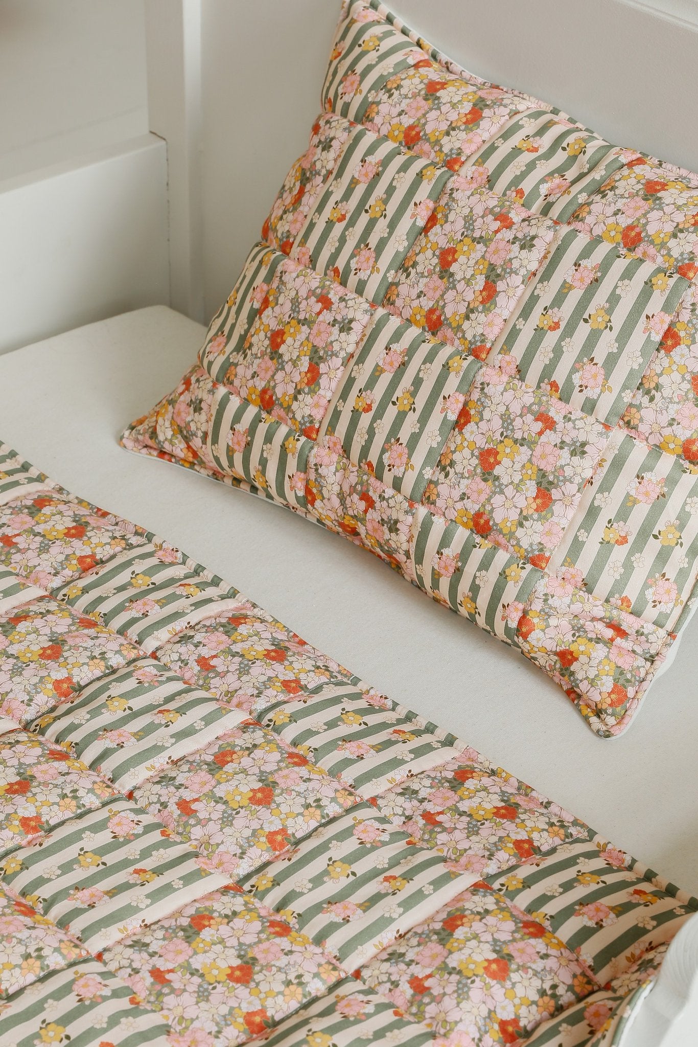5. Flat lay of Moi Mili cotton quilted patchwork blanket and pillow set in green garden pattern on white bed