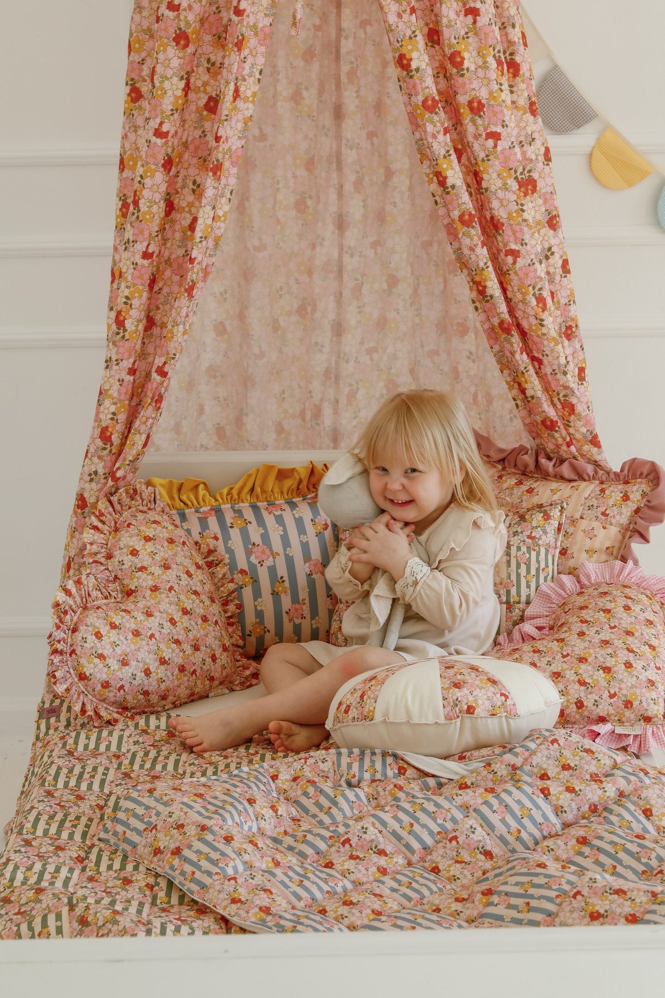 5. Child sitting on a bed with cotton quilted patchwork blanket and pillow set under a floral canopy