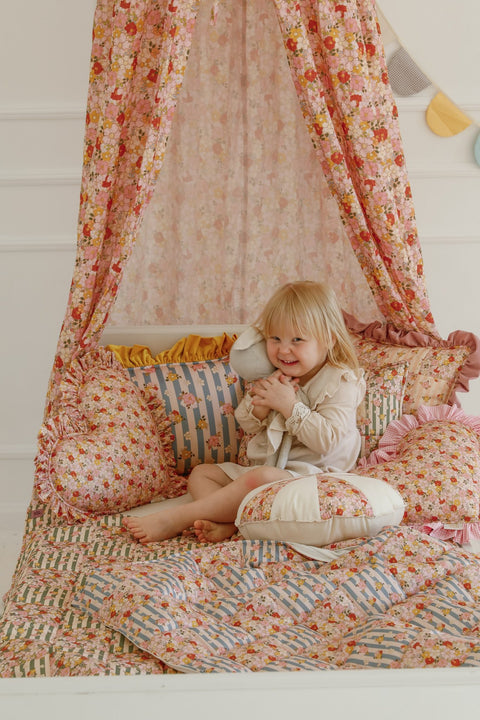 5. Child sitting on a bed with cotton quilted patchwork blanket and pillow set under a floral canopy
