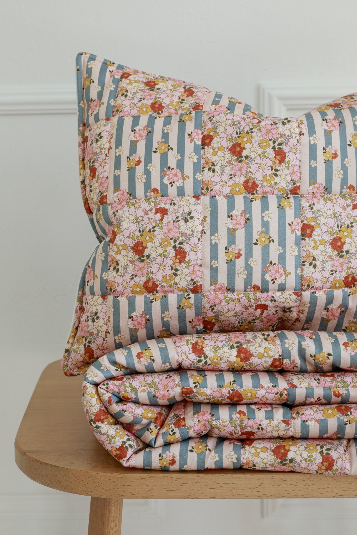 2. Close-up of folded Moi Mili cotton quilted patchwork blanket and pillow on wooden bench