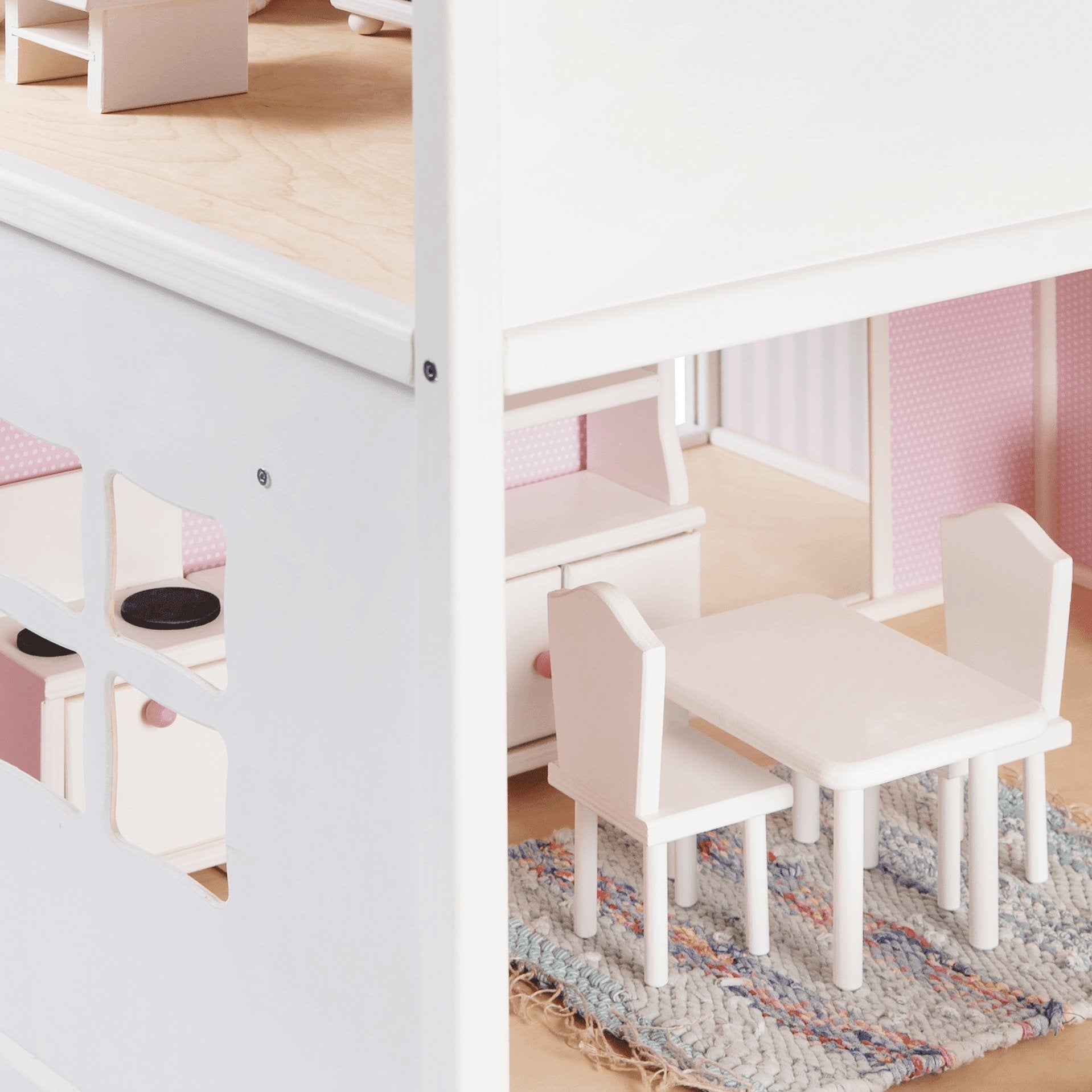 2. Close-up of dollhouse interior with white wooden furniture set on a woven rug, showing pink wallpaper and window detail