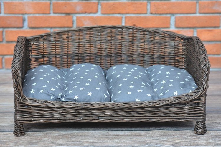2. Dark wicker pet bed with grey star-patterned cushion against brick wall, highlighting front view