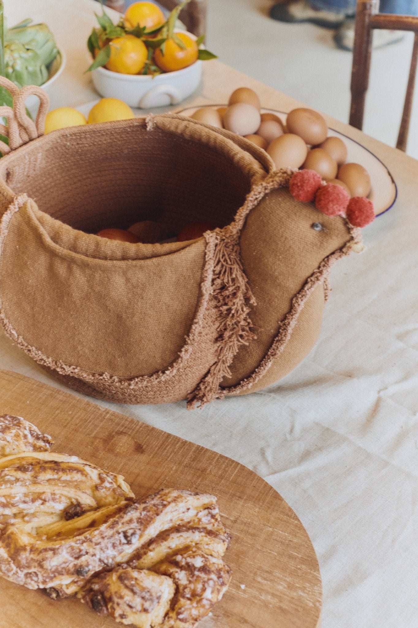 6. Lorena Canals chicken pouf on a table with eggs and pastries, enhancing a warm, rustic kitchen setting