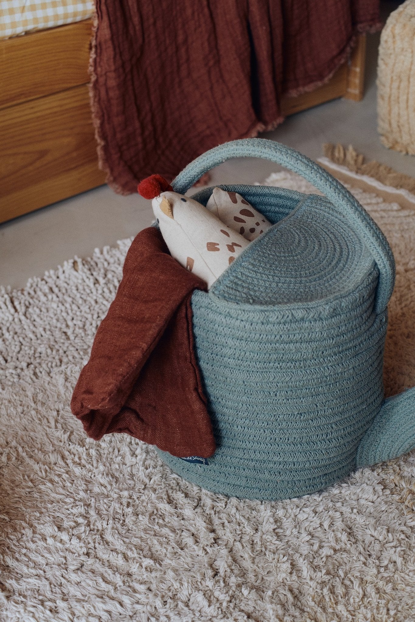 4. Blue decorative basket watering can with fabric items inside on textured rug