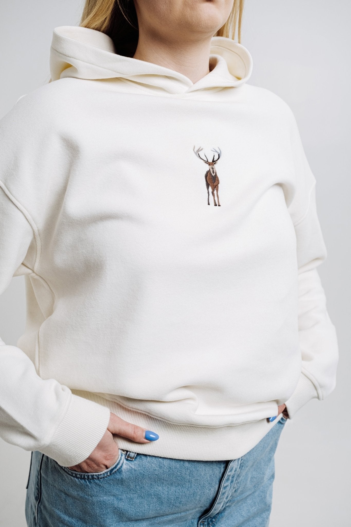 7. Close-up of woman wearing cream Sossu Deer Hoodie, highlighting relaxed fit and embroidery
