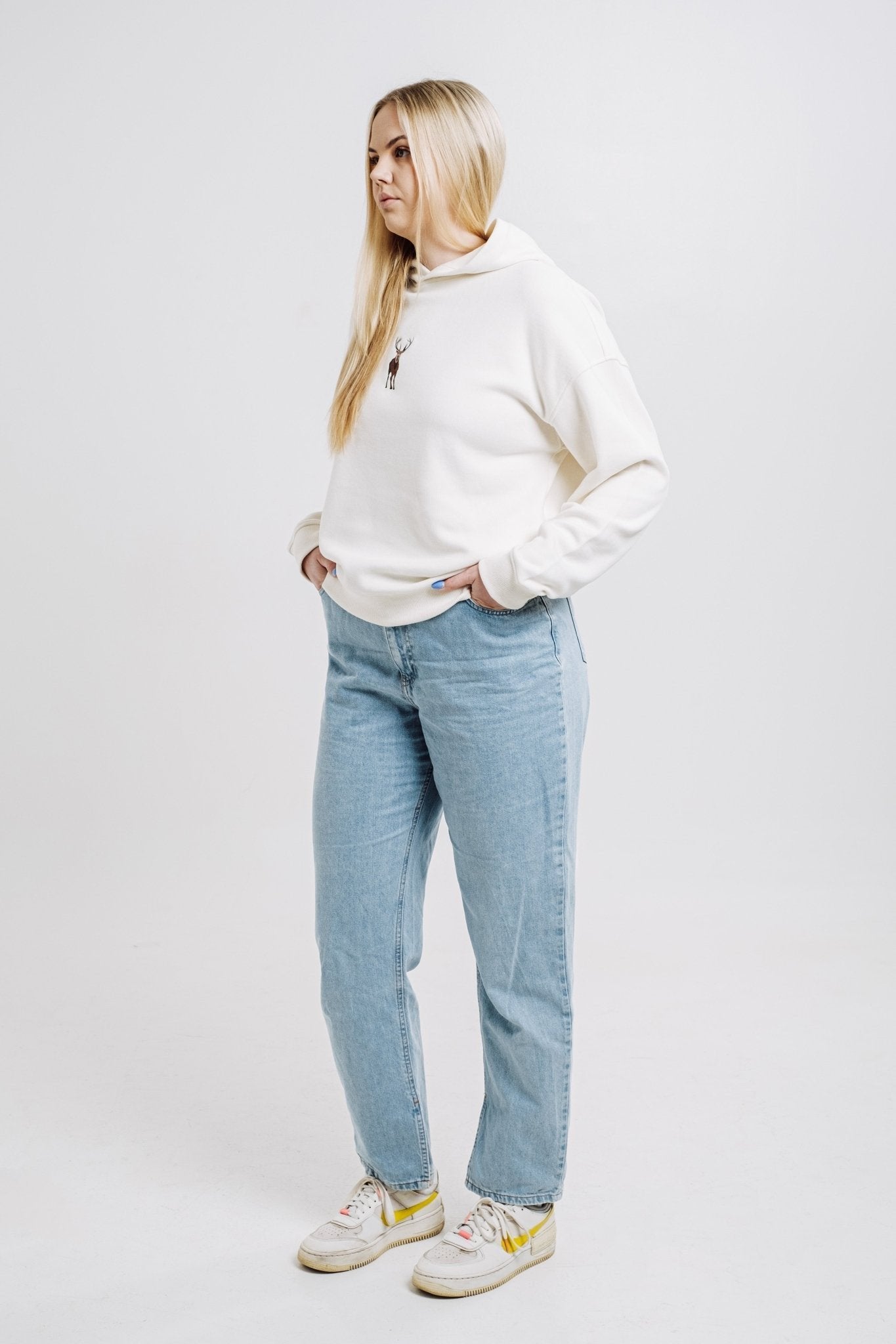 2. Woman wearing cream Sossu Deer Hoodie with relaxed fit and embroidered deer, styled with jeans in studio