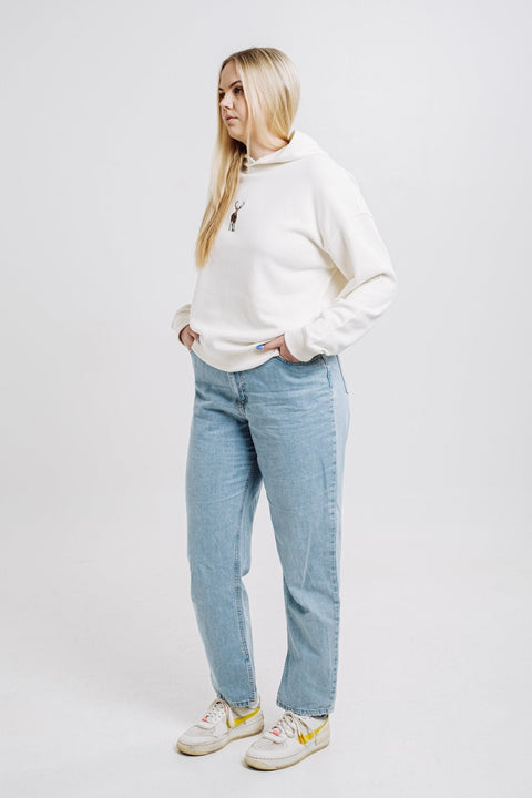 2. Woman wearing cream Sossu Deer Hoodie with relaxed fit and embroidered deer, styled with jeans in studio