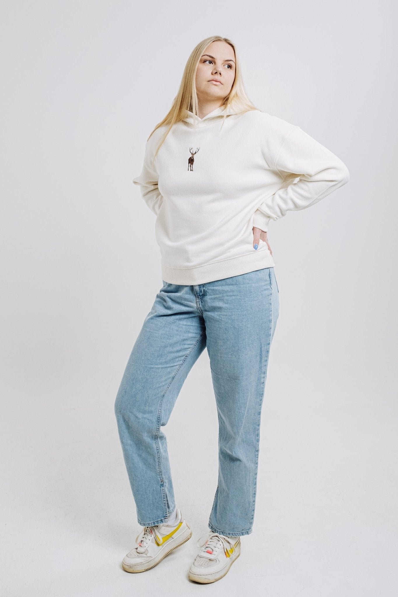 8. Woman posing in cream Sossu Deer Hoodie with embroidered deer, styled with jeans in studio