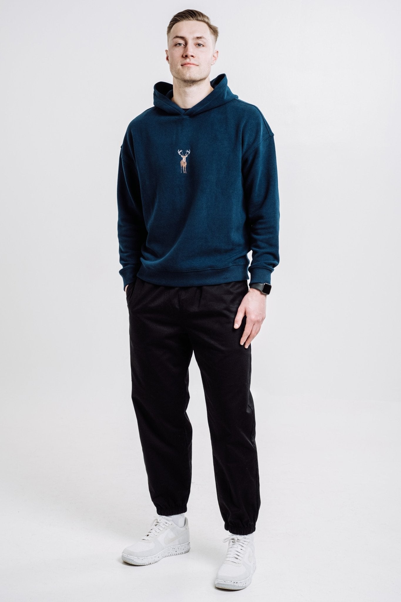 2. Full view of unisex Deer Hoodie in Indigo Blue worn by male model, styled with black pants and white sneakers