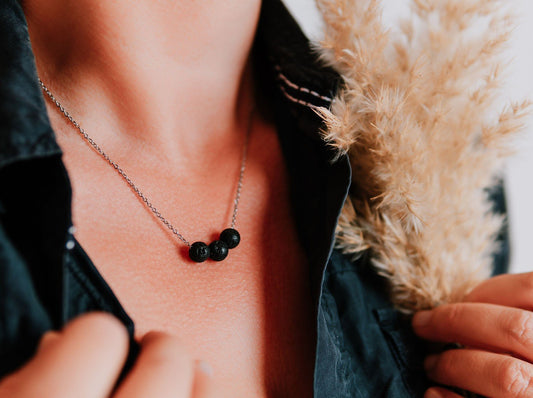 1. Woman wearing Canary Lava black lava stone necklace with golden chain, styled with a dark shirt and holding dried flowers