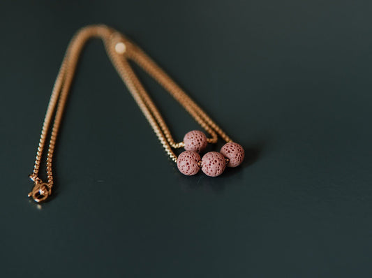 1. Pink lava stone necklace with three beads on a golden stainless steel chain, shown in a studio setting