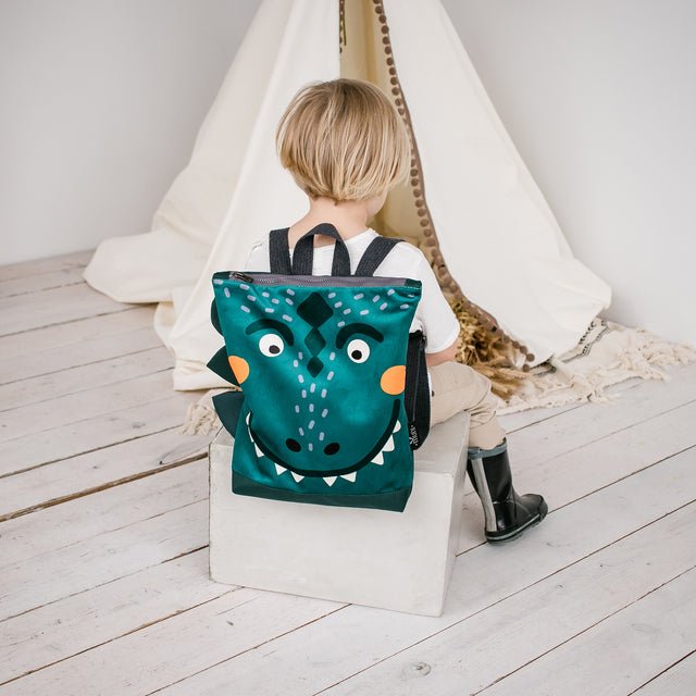 6. Child sitting with Muni dinosaur backpack in a cozy indoor setting