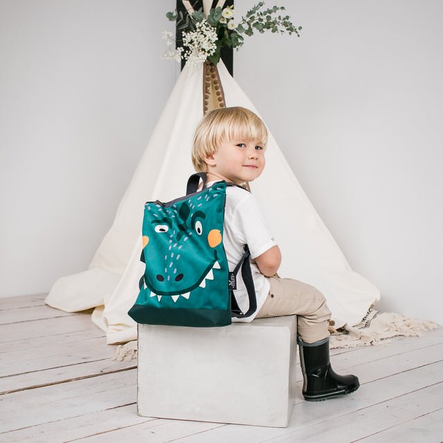 3. Child sitting with Muni dinosaur backpack in indoor setting