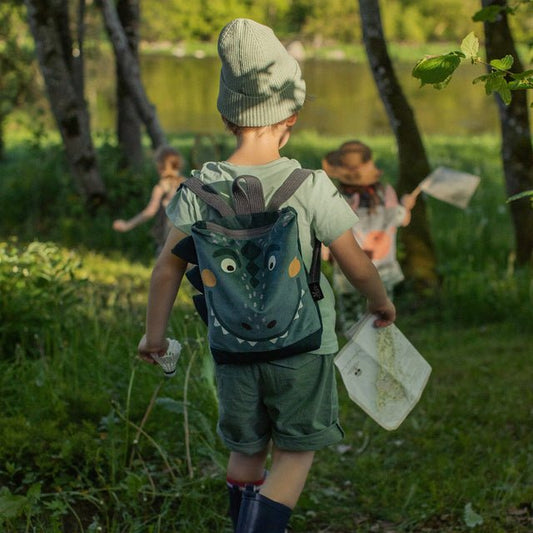 2. Child wearing Muni dinosaur backpack on outdoor adventure by the lake