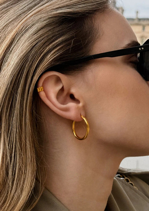 1. Woman wearing gold Django hoop earring by NO MORE, styled with sunglasses, showcasing elegant design and 24k gold vermeil finish