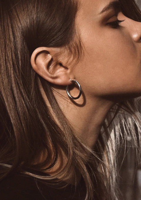 1. Woman wearing Django Hoops Silver earrings by NO MORE, crafted from 925 sterling silver, shown in profile with long brown hair