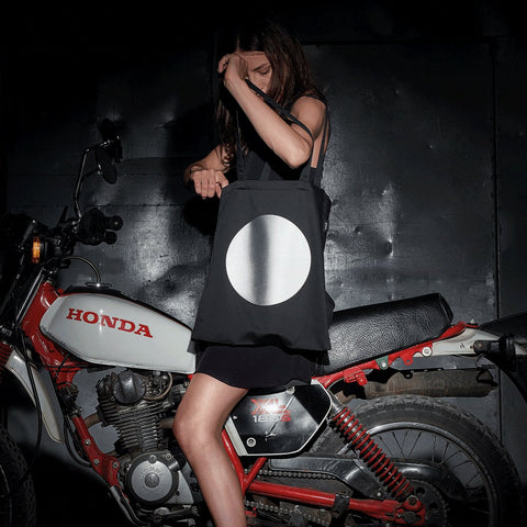 1. Women's MARCH Reflective Tote DOT in lifestyle setting, shown with motorcycle, highlighting reflective print
