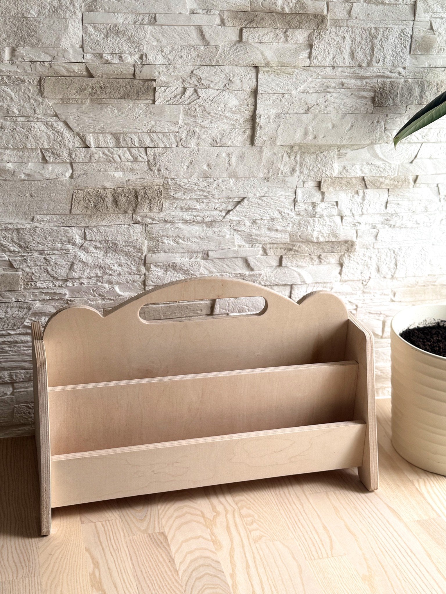 2. Montessori double-sided wooden book display on a wooden floor with a stone wall background, showcasing empty shelves and rounded handles