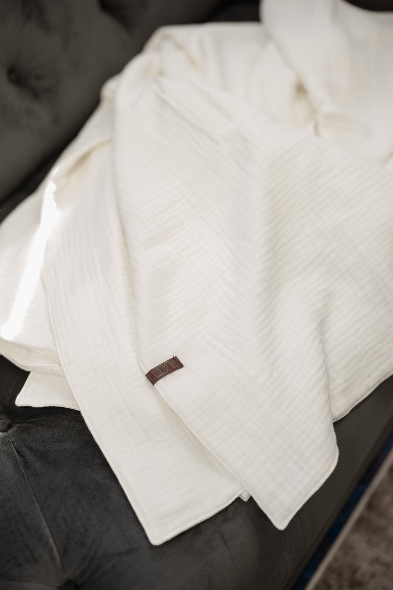 1. Soft muslin cotton blanket in ivory white by RÄTT, draped on a dark sofa, showcasing its ultra-soft and breathable texture