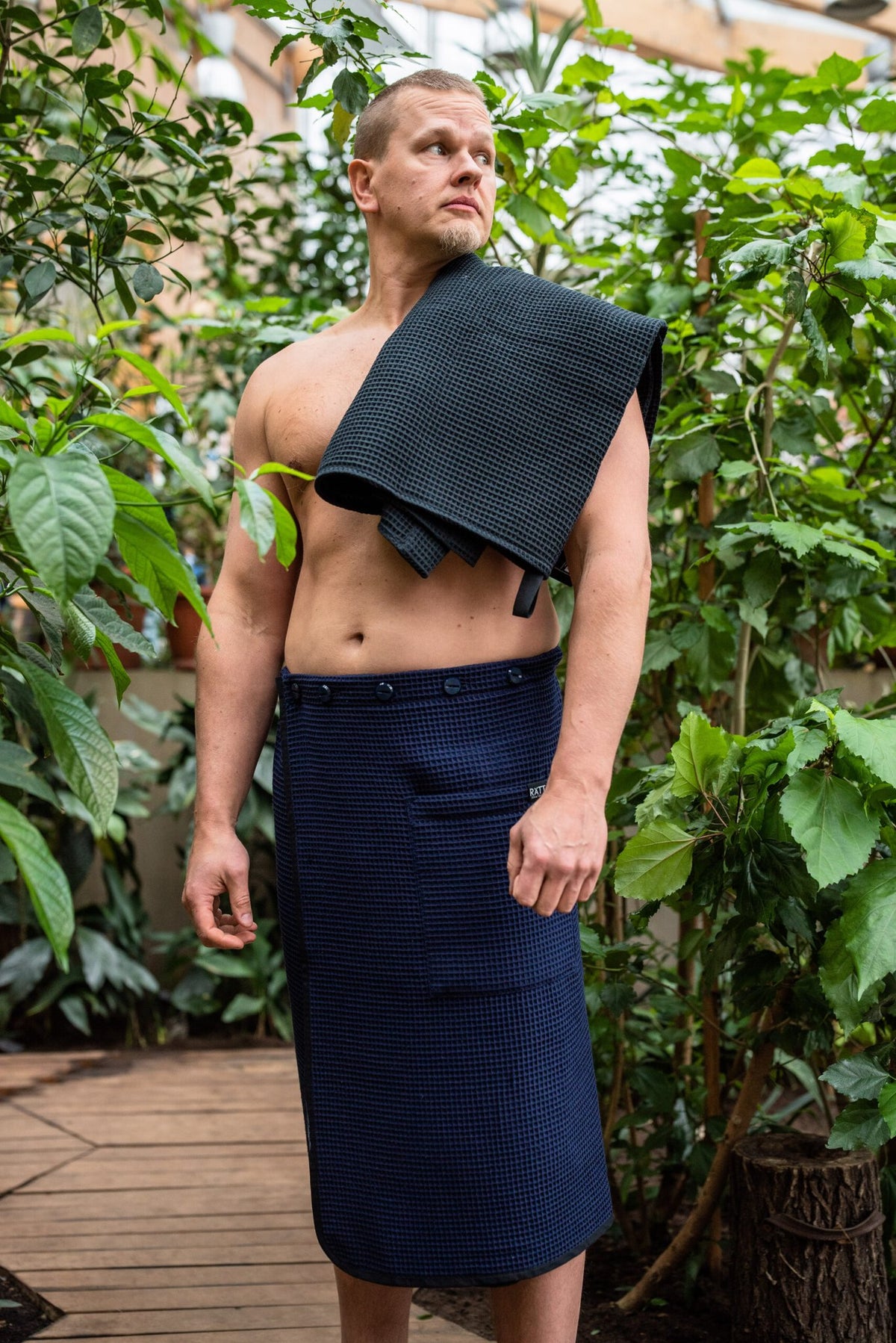 3. Men's black cotton waffle spa wrap by RÄTT, shown with matching towel over shoulder in garden setting