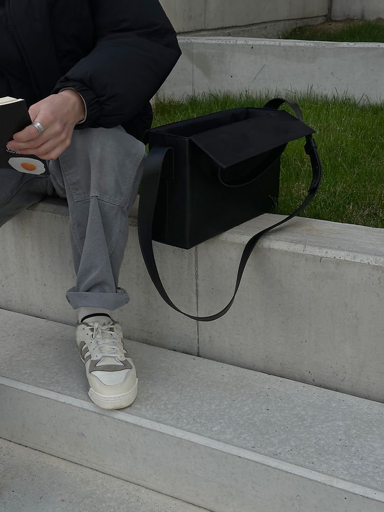 5. Black leather BOX Bag by RR on concrete steps, showing interior with sunglasses and red item inside