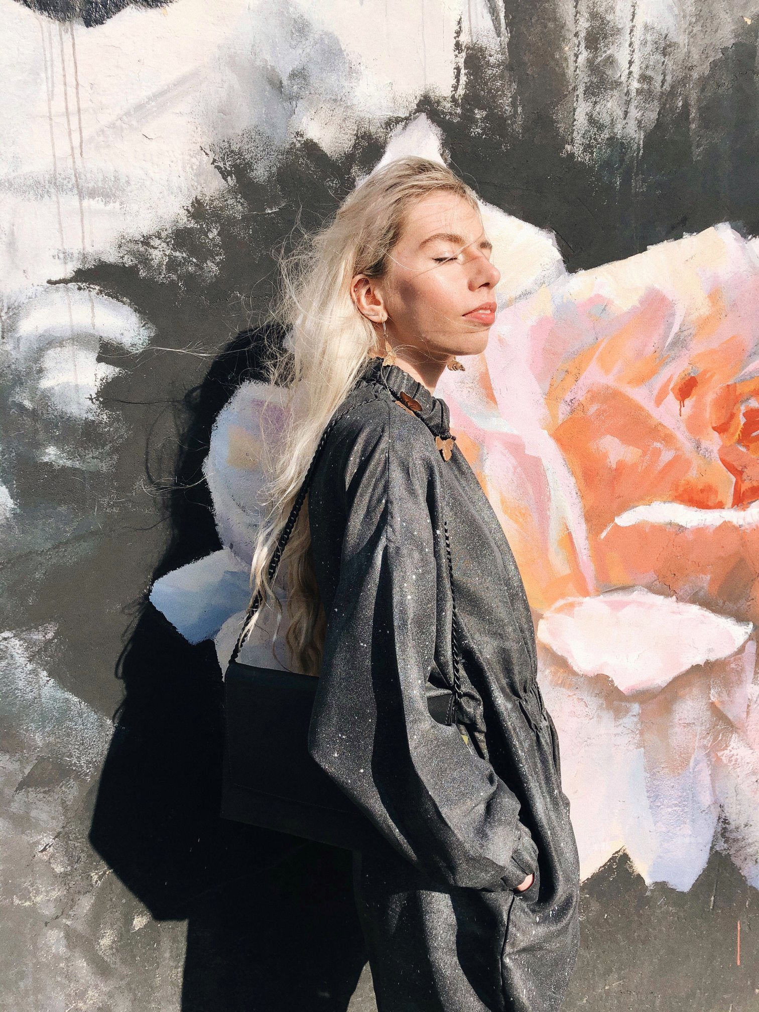 2. Woman wearing RR black matte leather chain shoulder bag against floral mural