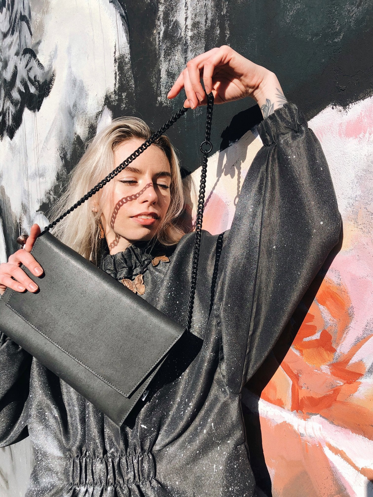 14. Woman posing with RR black chain shoulder bag, styled with metallic dress against floral mural
