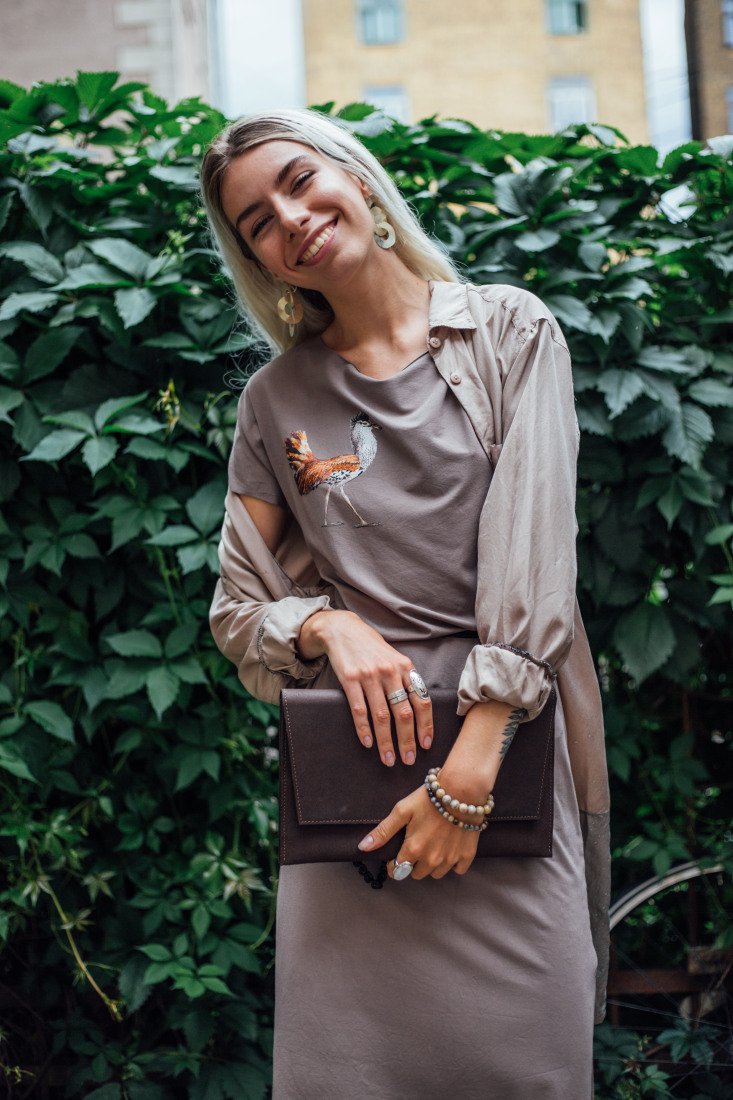 13. Woman smiling while holding RR dark brown chain shoulder bag, styled with taupe dress