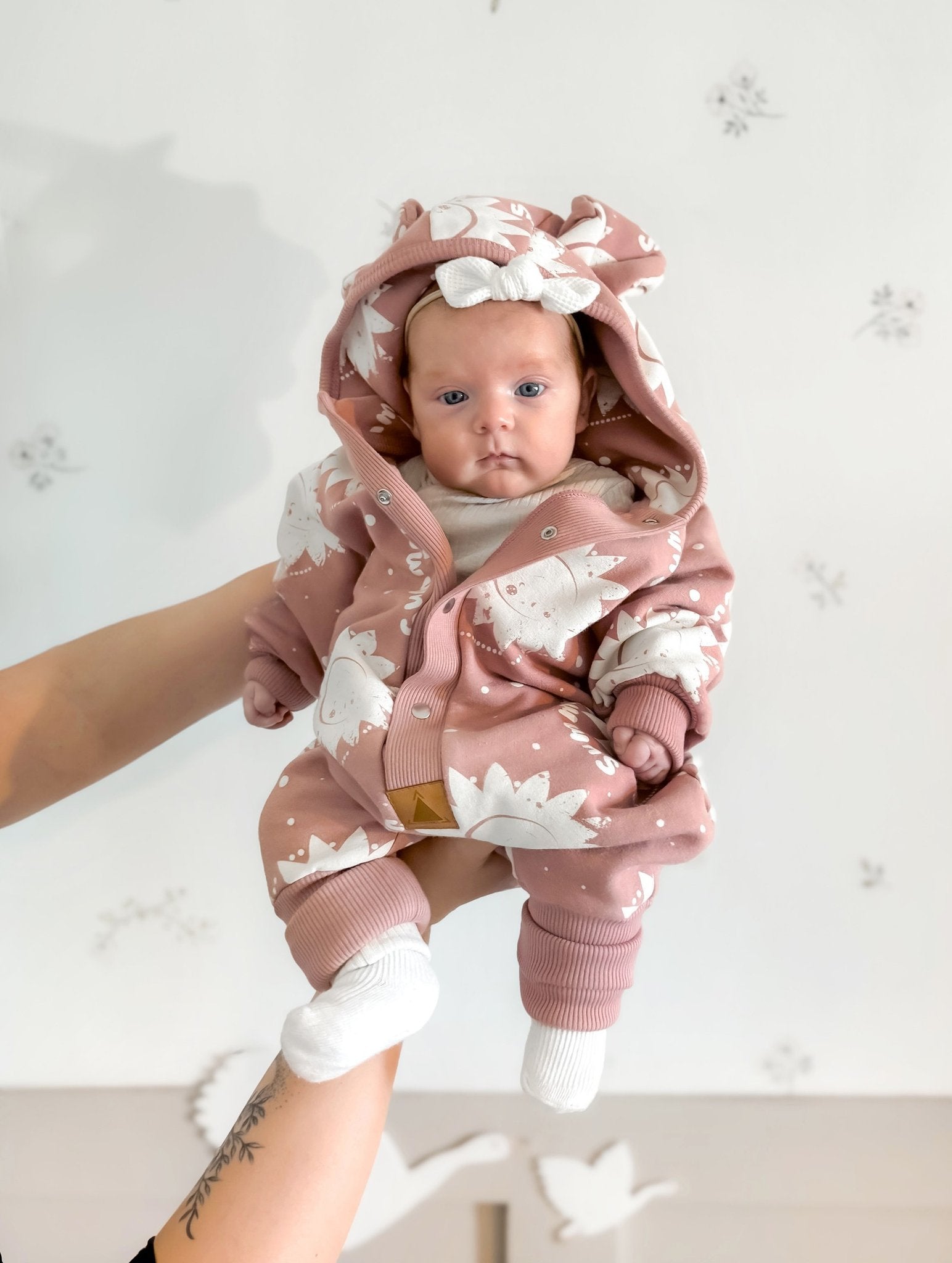 3. Baby held up wearing Zezuzulla pink suns eared jumpsuit with hood and white socks
