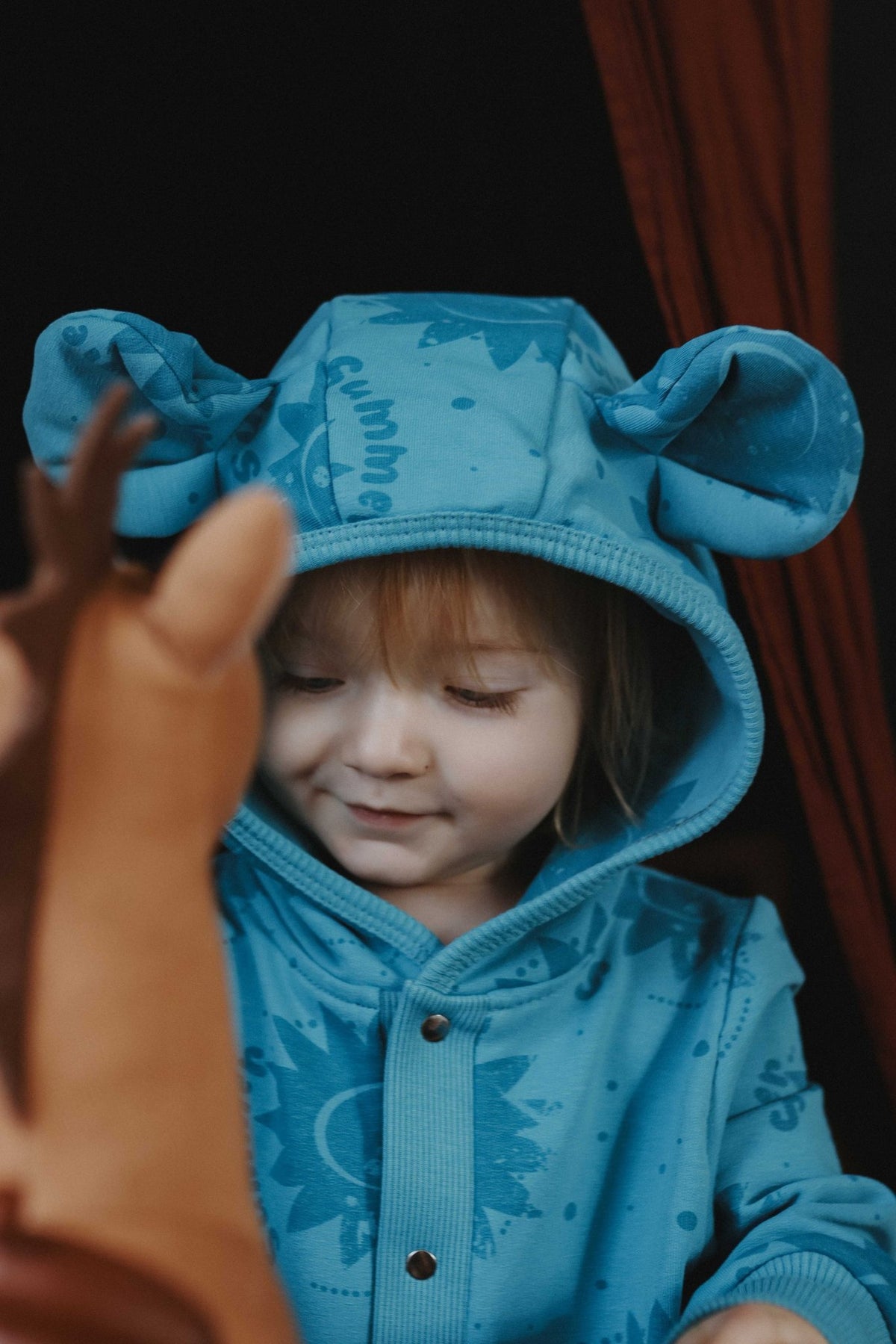1. Child wearing blue Zezuzulla eared jumpsuit with sun print, smiling while playing indoors