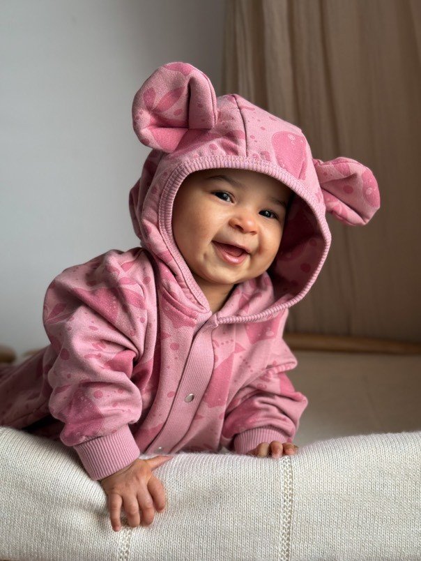 1. Smiling baby in pink eared jumpsuit with lemon print lying on soft surface