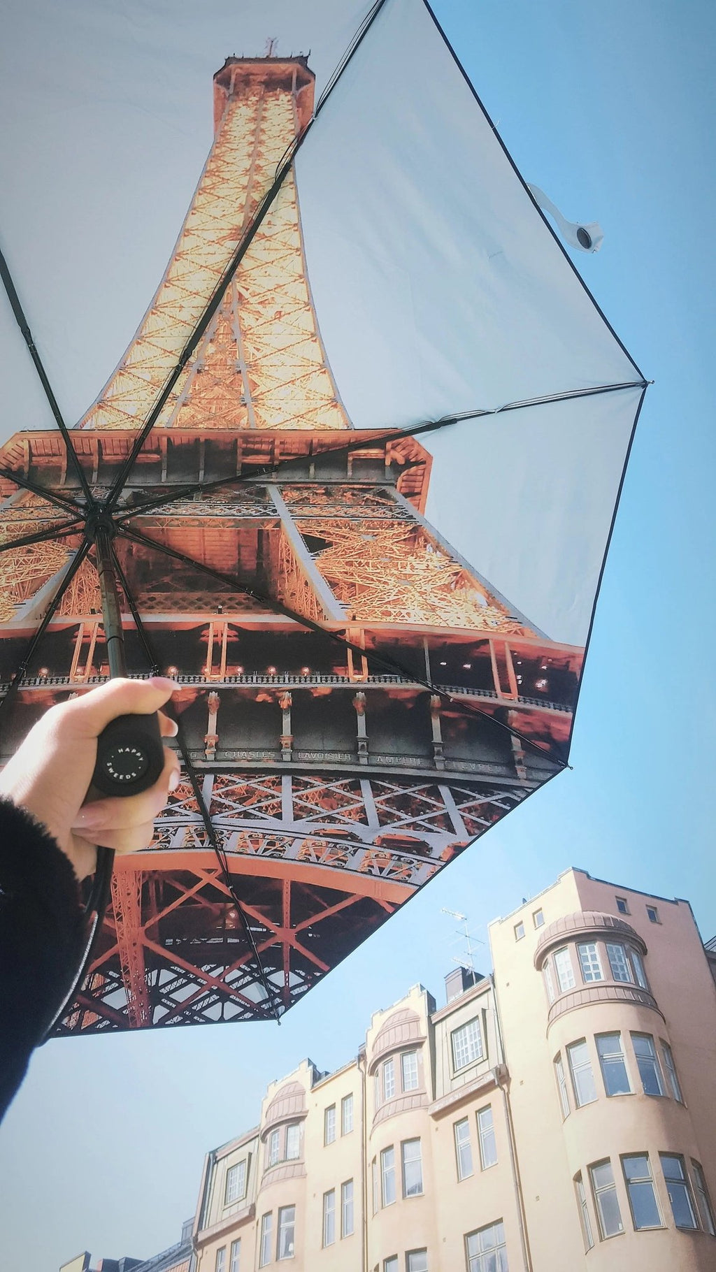 4. Person holding Eiffel Umbrella with Eiffel Tower print against a blue sky and urban backdrop