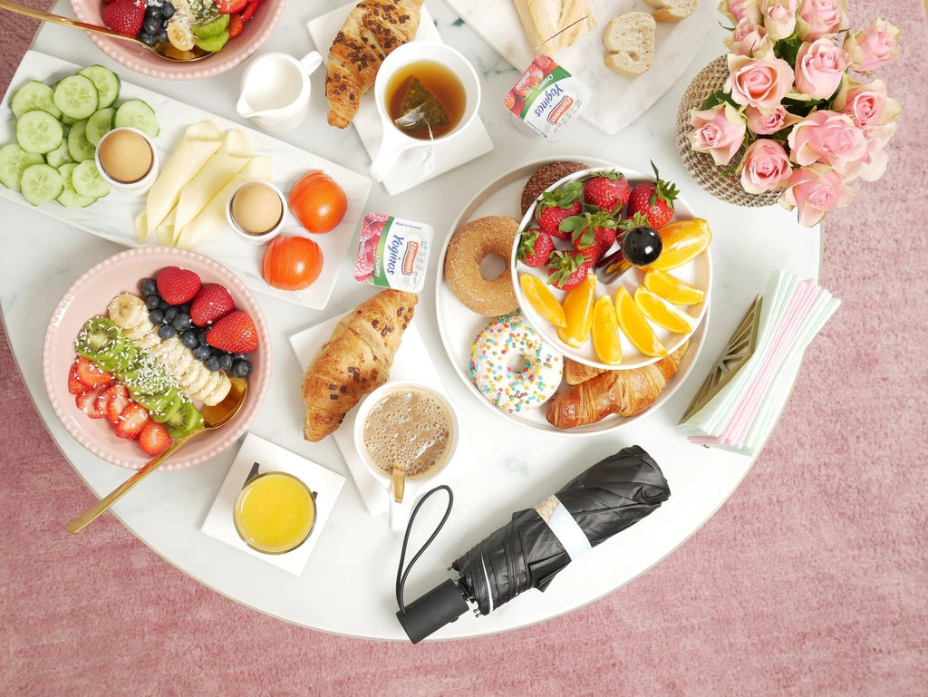 5. Flat lay of Eiffel Umbrella in black cover among a colorful breakfast spread on a pink table