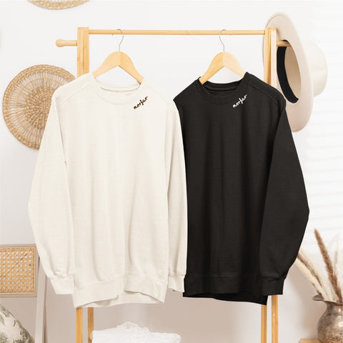 3. Beige and black sweatshirts with 'Morfar' embroidery on collars hanging on a wooden rack in a cozy room