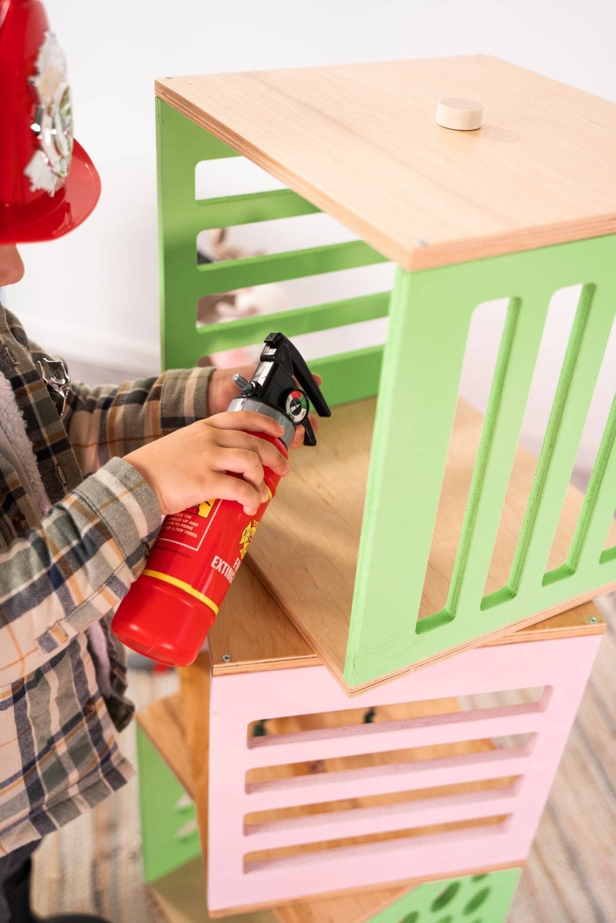 2. Close-up of child holding red toy extinguisher near green and pink Ewart Woods storage cubes