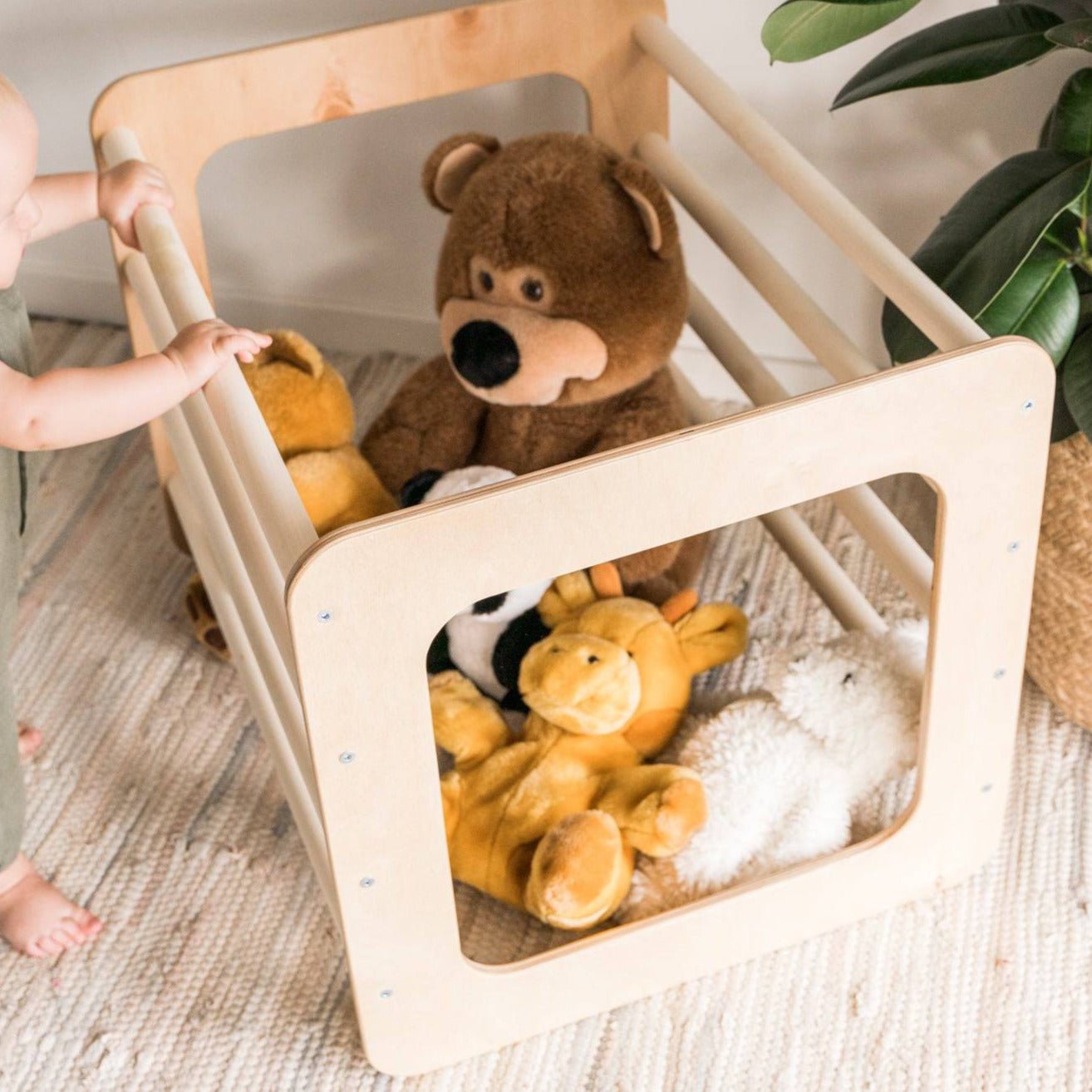 1. Toddler standing next to Ewart Woods square gym filled with plush toys on a woven rug
