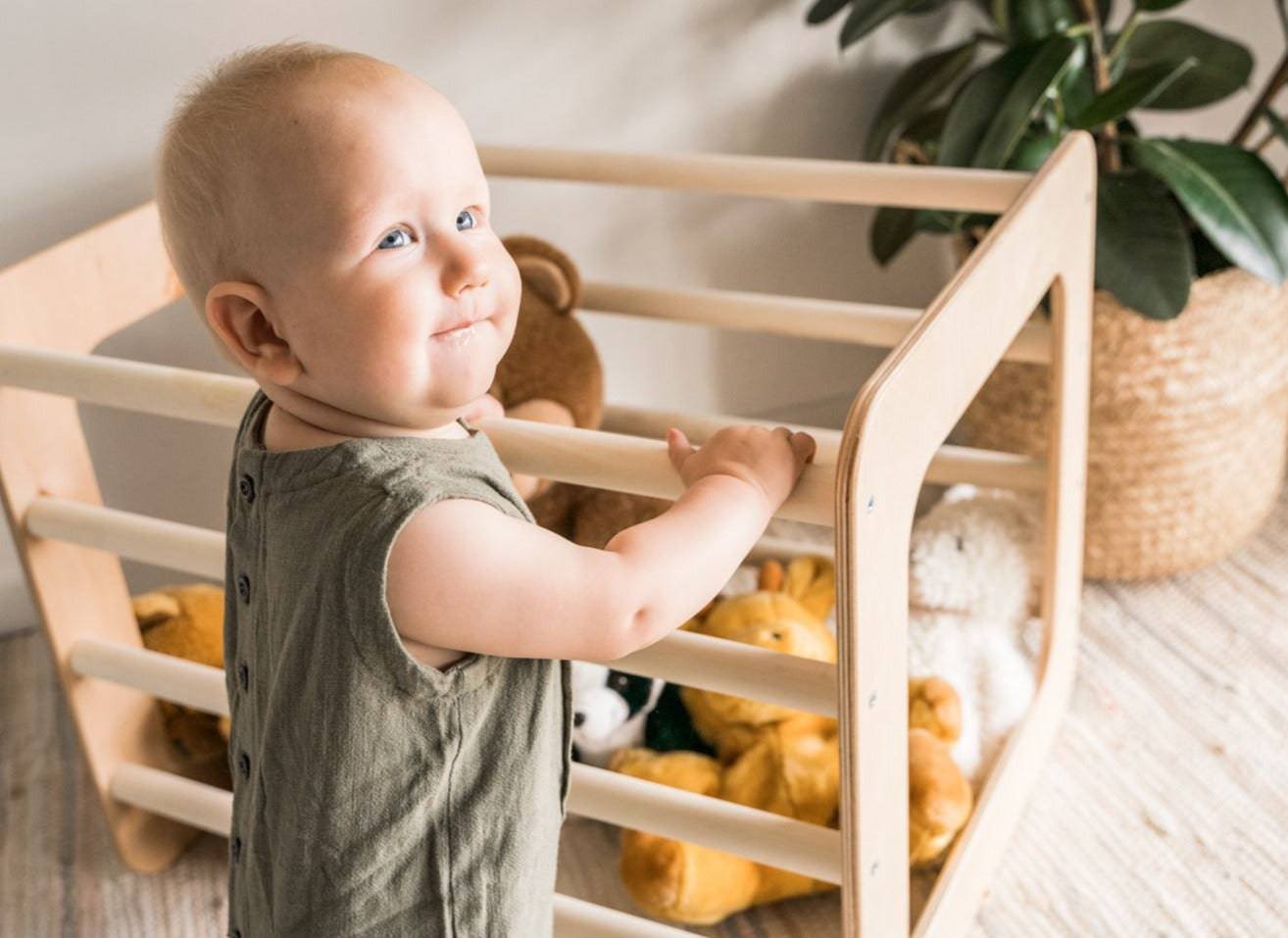 1. Smiling toddler holding Ewart Woods square gym filled with stuffed animals on a woven rug