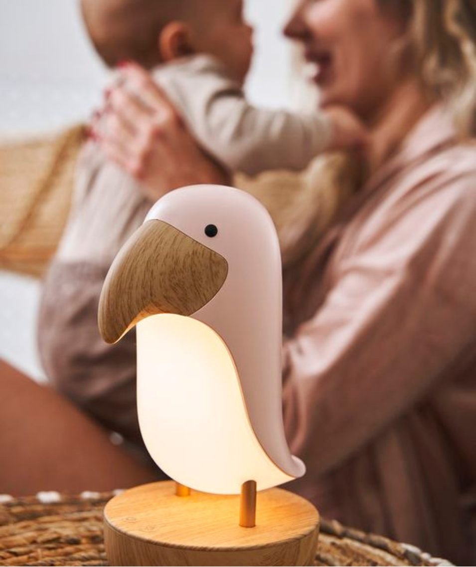 1. Woman holding baby with pink bird lamp illuminating the room, creating a warm atmosphere
