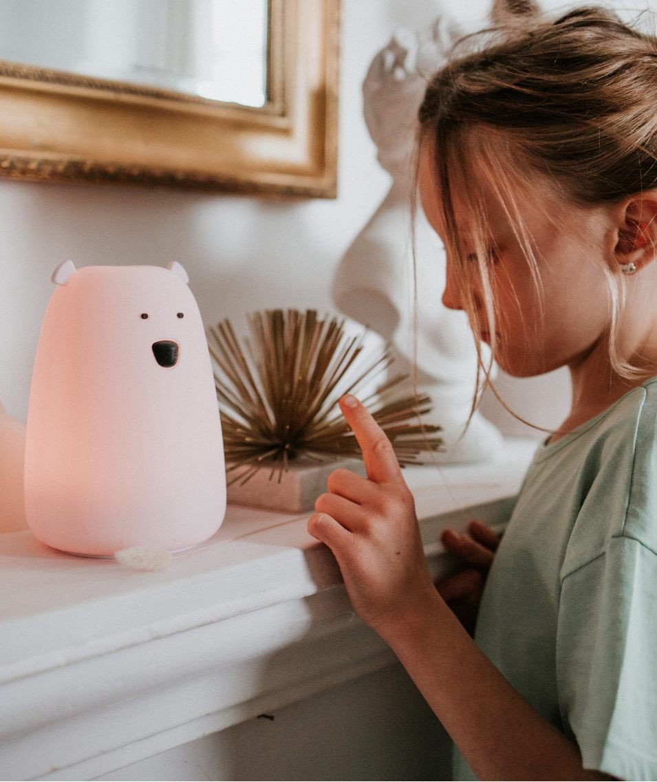 6. Child touching pink teddy bear-shaped lamp on mantelpiece, decorative background