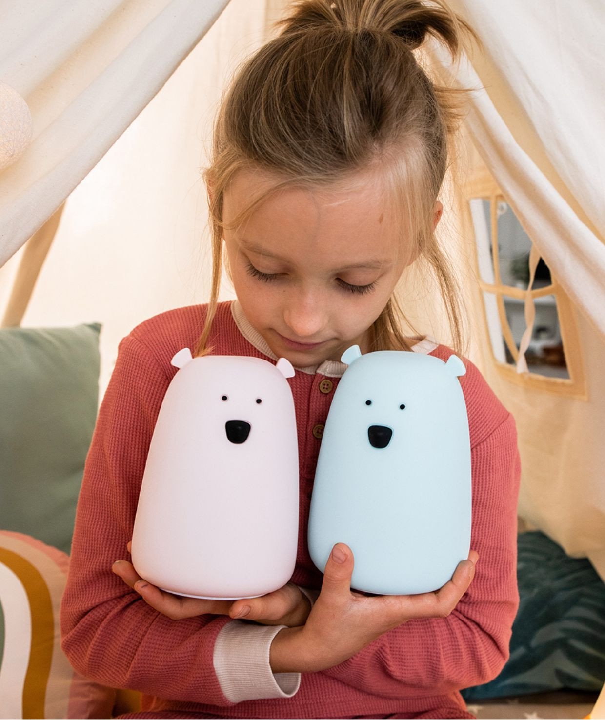 3. Young girl holding blue and white Big Bear silicone lamps by Rabbit & Friends in cozy tent setting