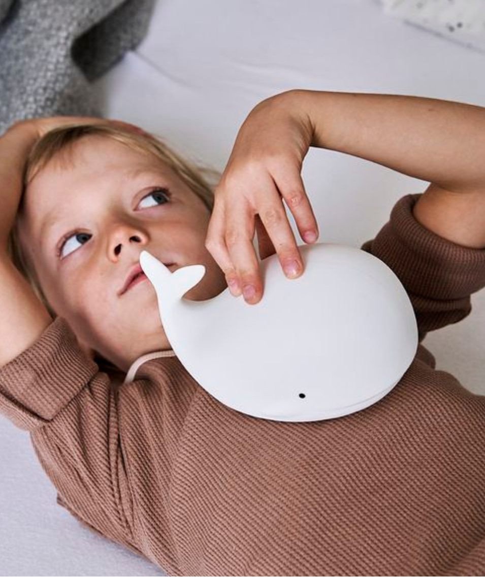 1. Child lying on bed holding white whale silicone lamp by Rabbit & Friends