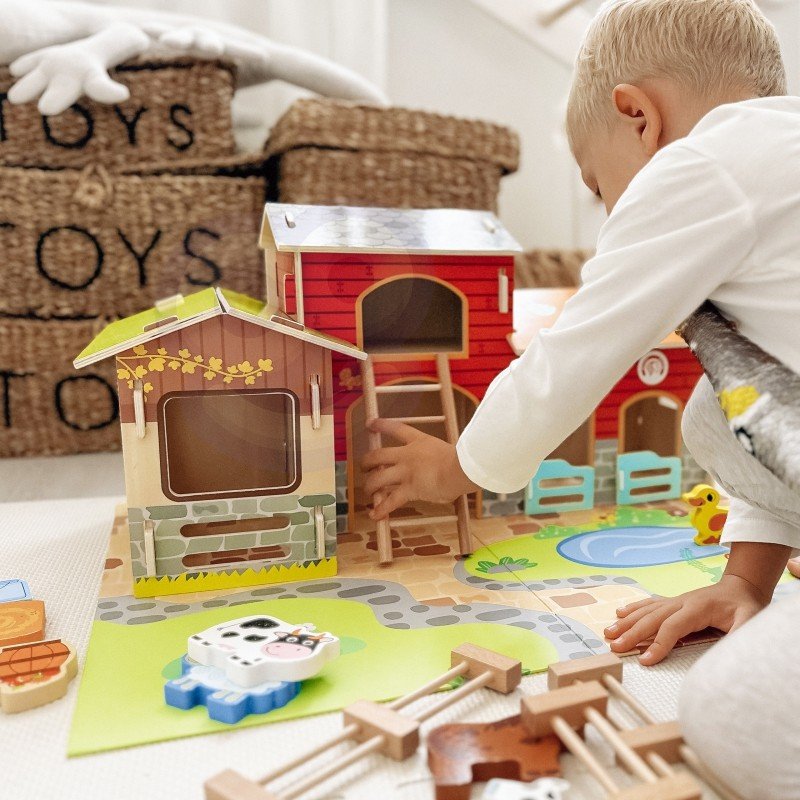 1. Child playing with Woopie Green Mega Farm set on floor, featuring barn and animal figurines in a nursery