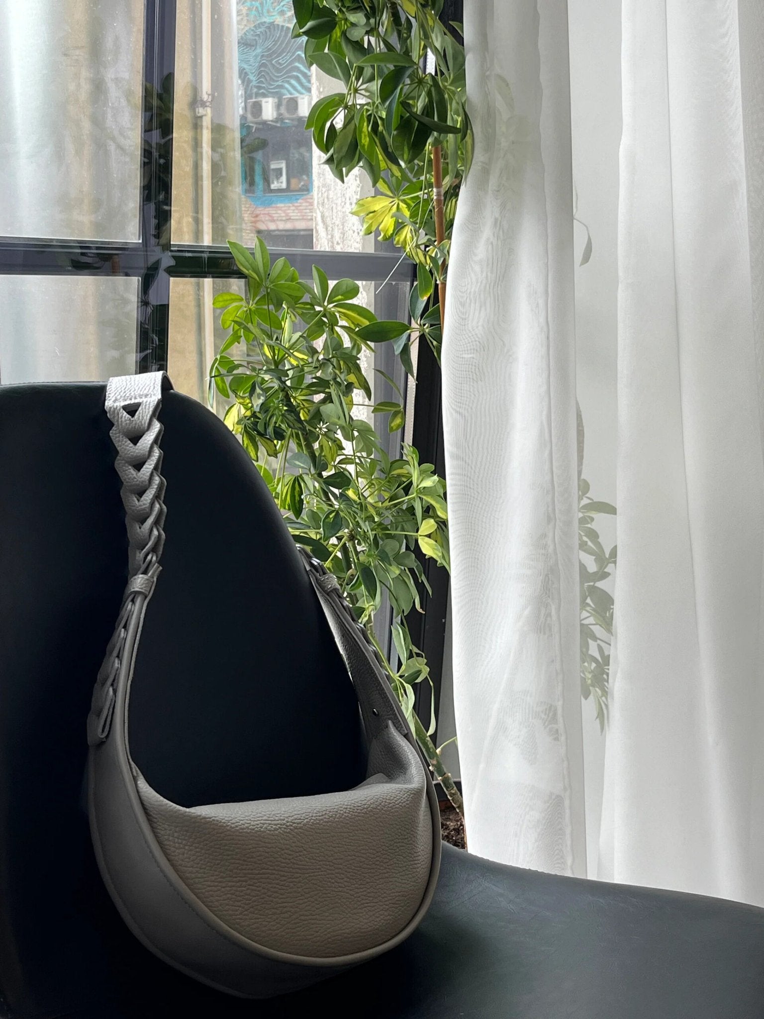 10. Grey Flora Leather Bag by Gerda Retter Design on black chair, with natural light and greenery